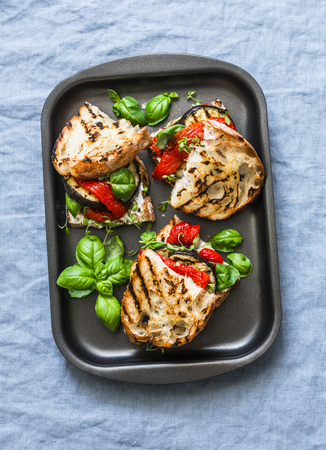 Summer grilled vegetables sandwiches. Eggplant, bell peppers, ciabatta, yogurt sauce, basil sandwiches in baking sheet on blue background, top view. Vegetarian diet food conceptの写真素材