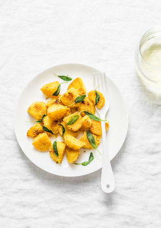 Crispy polenta crust potatoes baked with sage butter and a glass of white wine on a light background, top viewの写真素材