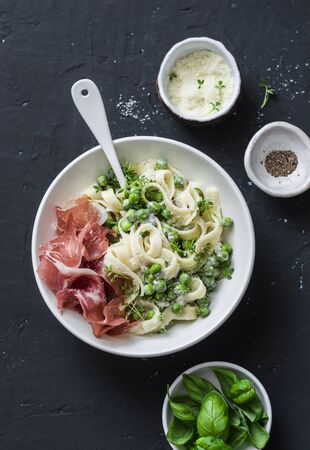 Fettuccine pasta with creamy sauce, green peas and prosciutto on dark background, top viewの写真素材