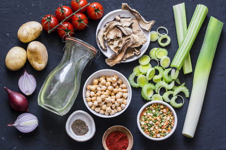 Ingredients for detox soup - bouillon in bottle, celery, chickpeas, leeks, tomatoes, red onions, spices on dark background, top view. Flat layの写真素材