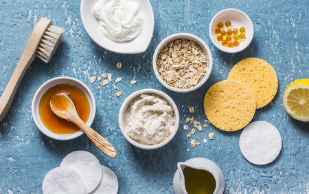 Homemade beauty products concept. Natural moisturizing, nourishing, cleansing face mask - coconut oil, oatmeal, natural yogurt, vitamin E, honey, face brush, sponge on blue background, top view. Flat layの写真素材