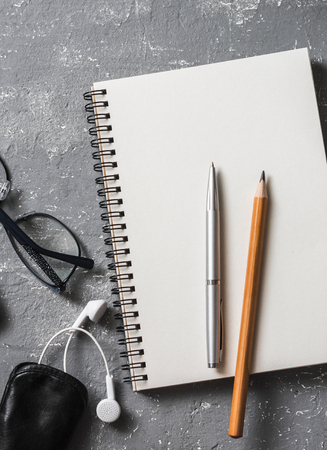Flat lay office workplace. Business or education accessories - blank notepad glasses, pens, pencils, headphones on grey background, top view. Free space for textの写真素材