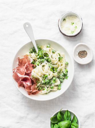 Fettuccine pasta with creamy sauce, green peas and prosciutto on light background, top viewの写真素材