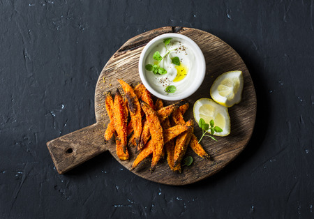 Crispy cornmeal sweet potato fries rustic wooden cutting board on dark background, top viewの写真素材