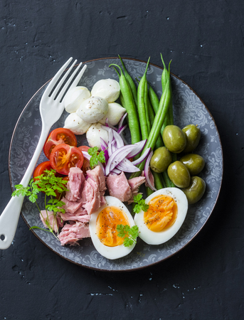 Balanced breakfast or snack - plate of canned tuna, green beans, mozzarella cheese, tomatoes, boiled egg, olives on a dark background, top viewの写真素材