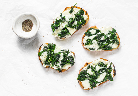 Mozzarella cheese creamy spinach bruschetta on light background, top view. Delicious healthy breakfast, snack, appetizer, tapasの写真素材