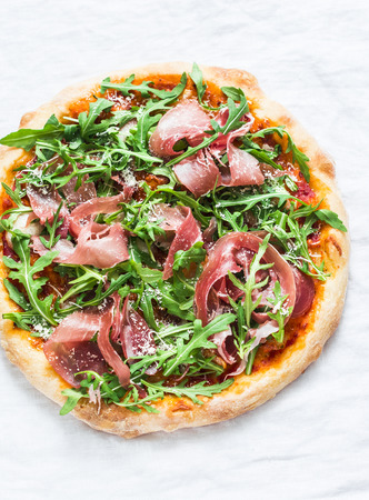Prosciutto arugula homemade pizza on light background, top view. Delicious appetizers, snack, tapas in mediterranean style. Free spaceの写真素材