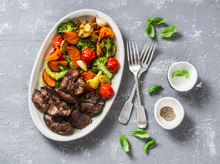 Baked seasonal vegetables - sweet potatoes, broccoli cabbage, sweet peppers, cherry tomatoes, beets, garlic, zucchini and chicken liver - served lunch on grey background, top viewの写真素材