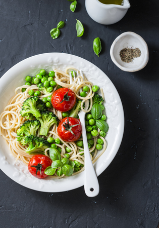 Veggie pasta. Vegetarian lunch - spaghetti with broccoli cabbage, green peas and cherry tomatoes on dark background, top view. Healthy  food conceptの写真素材
