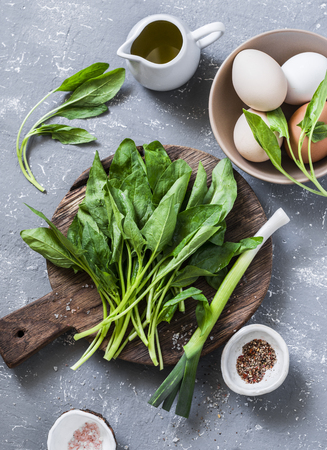 Ingredients for green shakshuka - fresh spinach, garlic, ramson and organic farm eggs on grey background, top viewの写真素材