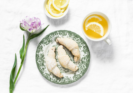Cup of green tea with lemon, mini croissants, tulip flower - morning cozy still life on a white background, top view.Flat layの写真素材