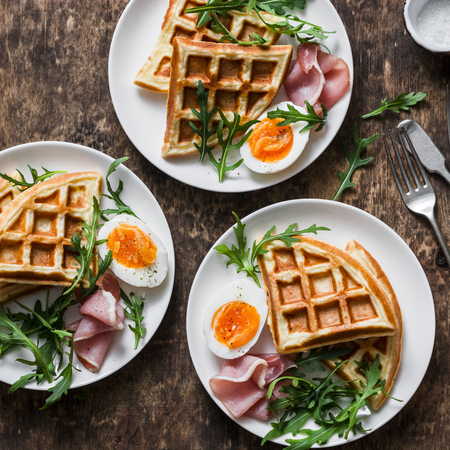 Delicious savory breakfast on a wooden background - boiled eggs, potato waffles and ham, top viewの写真素材