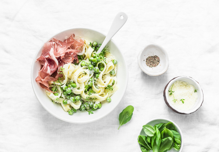Fettuccine pasta with creamy sauce, green peas and prosciutto on light background, top viewの写真素材