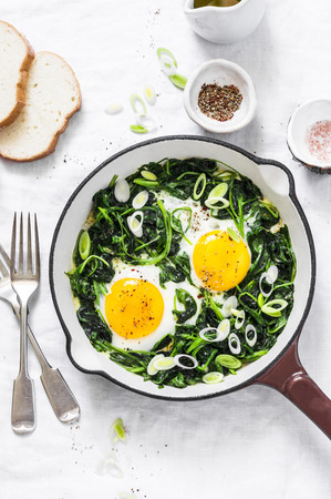 Green shakshuka. Fried eggs with fresh spinach, ramson, leek in a cast iron skillet on a white background, top viewの写真素材