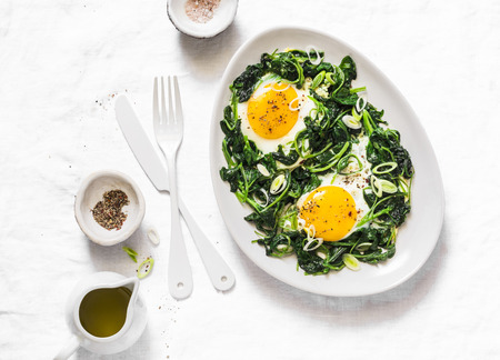Fried organic farm eggs with spinach - healthy breakfast on a light background, top viewの写真素材