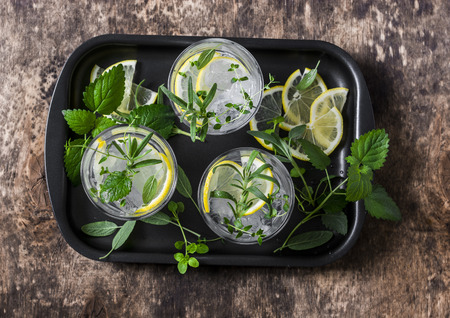 Garden herbs lemonade. Infused water with lemon, rosemary, thyme, sage and mint on wooden background, top view. Summer cool drinkの写真素材