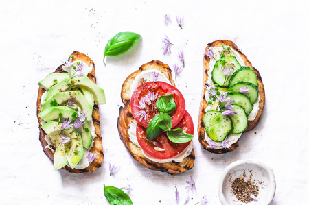 Summer variations of sandwiches - with cream cheese, avocado, tomato and cucumber on a light background, top view. Healthy diet food concept. Flat lay, copy spaceの写真素材