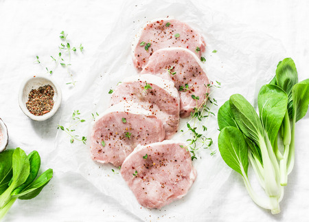 Fresh raw pork chops with spices and thyme and cabbage Bok Choi on light background, top view. Ingredients for cookingの写真素材