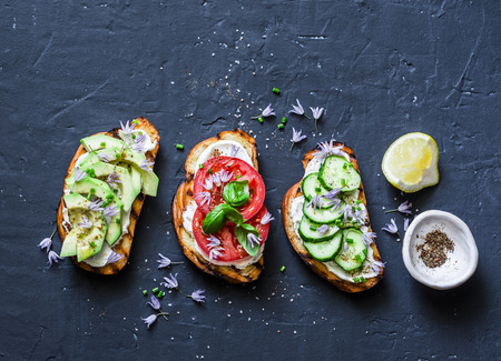Variations of sandwiches - with cream cheese, avocado, tomato and cucumber on a dark background, top view. Healthy diet food concept. Flat layの写真素材