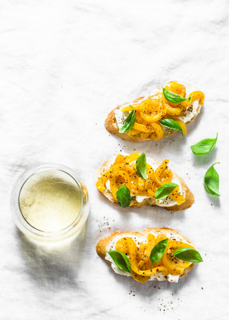 Cream cheese, roasted yellow bell pepper, basil bruschetta and white  wine on light background, top view. Flat lay, copy spaceの写真素材
