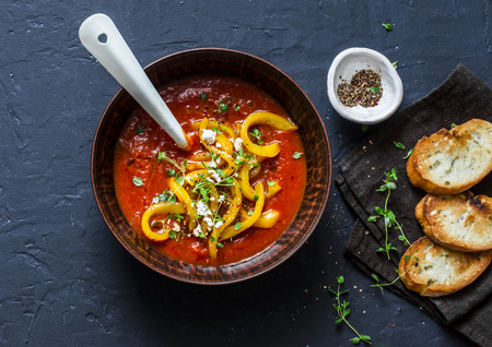 Tomatoes soup with roasted bell yellow pepper and goat cheese. Delicious vegetarian food on dark background, top viewの写真素材
