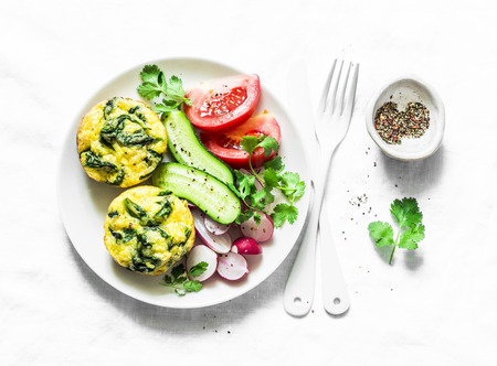 Mini spinach cheddar frittata and vegetables salad on light background, top view. Breakfast table flat lay. Copy spaceの写真素材