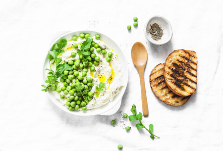 Fresh ricotta cheese with green peas, olive oil, pepper and herbs on a light background, top view. Healthy diet food - delicious breakfast, snack, appetizers.Flat layの写真素材