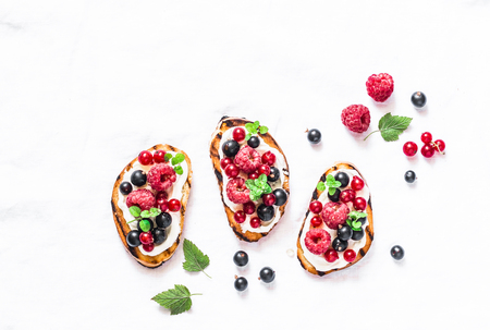 Berries bruschetta on a light background, top view. Sandwiches with cream cheese, raspberries, red and black currants. Delicious breakfast, snack. Flat layの写真素材