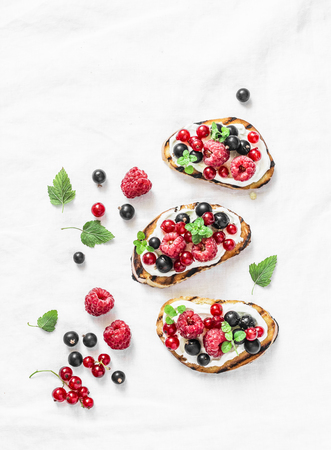 Berries bruschetta on a light background, top view. Sandwiches with cream cheese, raspberries, red and black currants. Delicious breakfast, snack. Flat layの写真素材
