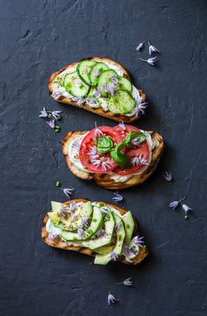 Sandwiches with cream cheese, avocado, tomato and cucumber on a dark background, top view. Healthy diet food concept. Flat layの写真素材