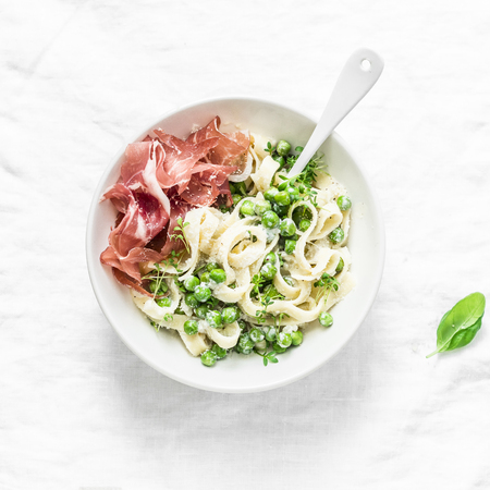 Fettuccine pasta with creamy sauce, green peas and prosciutto on light background, top viewの写真素材