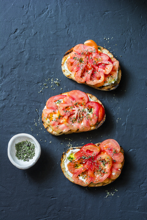Heirloom tomatoes, feta cheese, oregano bruschetta on a dark background, top view. Delicious appetizers, tapas, snackの写真素材