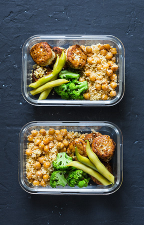 Healthy lunch box - spicy couscous with chickpeas, broccoli, green beans and turkey meatballs on dark background, top view. Copy spaceの写真素材