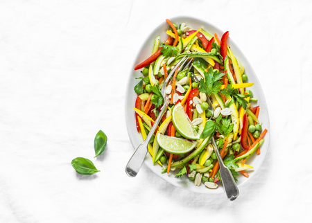 Raw vegetables slaw salad on light background, top view. Zucchini, bell peppers, carrots, squash, green peas salad. Vegetarian foodの写真素材