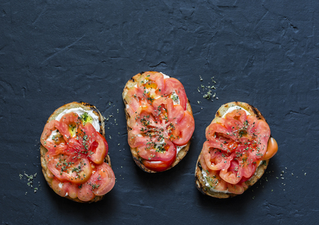 Tomatoes, cream cheese, oregano bruschetta on a dark background, top view. Delicious appetizers, tapas, snack. Copy spaceの写真素材