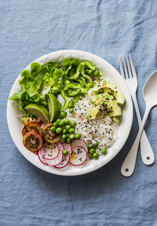 Coconut rice and vegetables buddha bowl. Vegetarian healthy lunch - rice, salad, avocado, radish, tomatoes on a blue background, top viewの写真素材