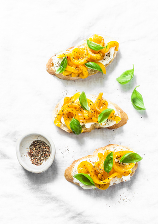Cream cheese, roasted yellow bell pepper, basil bruschetta on  on light background, top view. Copy space, flat layの写真素材