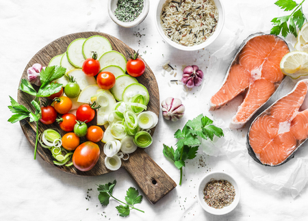 Ingredients for  healthy, balanced lunch - salmon and vegetables. Red fish, zucchini, squash, cherry tomatoes, leek, wild rice, spices on a light background, top view. Flat layの写真素材