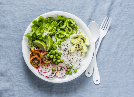 Coconut rice and vegetables buddha bowl. Vegetarian healthy lunch - rice, salad, avocado, radish, tomatoes on a blue background, top viewの写真素材