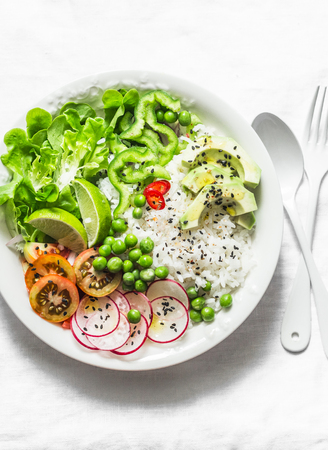 Coconut rice and vegetables buddha bowl. Vegetarian healthy lunch - rice, salad, avocado, radish, tomatoes on a light background, top viewの写真素材