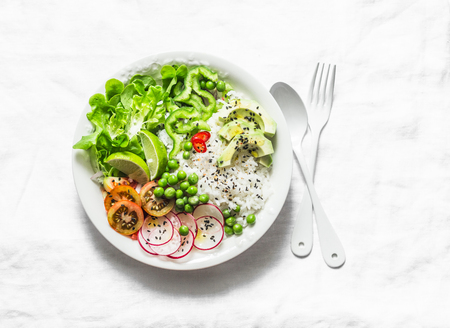 Coconut rice and vegetables buddha bowl. Vegetarian healthy lunch - rice, salad, avocado, radish, tomatoes on a light background, top viewの写真素材