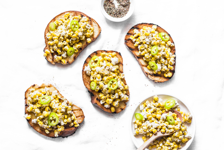Corn and goat cheese grilled bruschetta on a light background, top view. Delicious snack or appetizersの写真素材