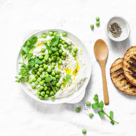 Fresh labne with green peas, olive oil and spices. Healthy diet breakfast, snack, appetizer on a light background, top viewの写真素材