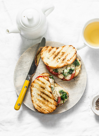 Hot grilled tomatoes, spinach, mozzarella sandwiches and green tea - healthy breakfast, snack on a light background, top viewの写真素材