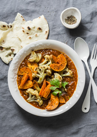 Roasted curry vegetables. Sweet potatoes, cauliflower, carrots, onions, pumpkin with curry sauce on grey background, top view. Vegetarian food conceptの写真素材