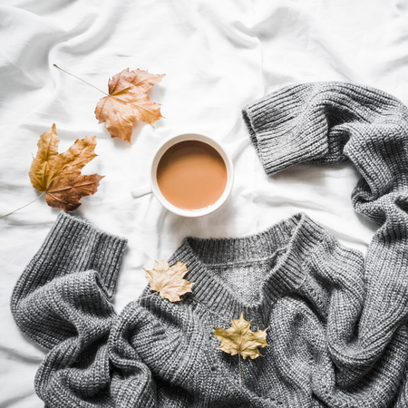 Cup of coffee, gray warm knitted sweater oversize, yellow dry leaves on the bed - cozy home still life, top viewの写真素材