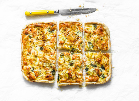 Salmon, leek, spinach, cheese puff pastry tart, pie on light background, top viewの写真素材