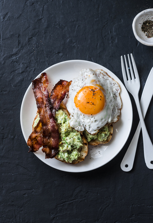 Healthy nutritious breakfast - avocado toast, bacon and fried egg on dark background, top viewの写真素材