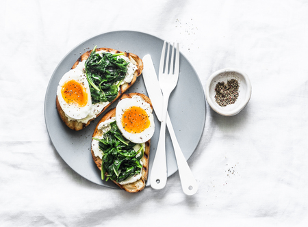 Fried spinach, labne and boiled eggs sandwiches - delicious healthy breakfast or snack on a light background, top viewの写真素材
