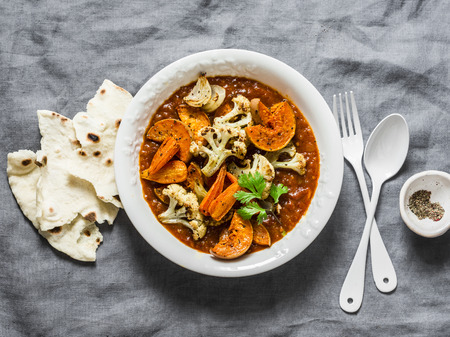Roasted curry vegetables. Sweet potatoes, cauliflower, carrots, onions, pumpkin with curry sauce on grey background, top view. Vegetarian food conceptの写真素材